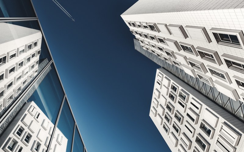 a low angle shot of an airplane in the sky over a white building, airplane over white buildings 4k
