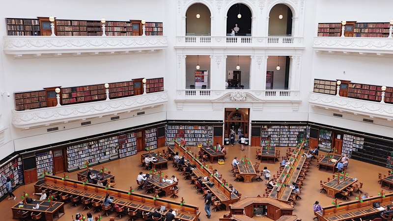 interior view of the state library of victoria with bookcases and people sitting at desks, ornate library with books and people 4k