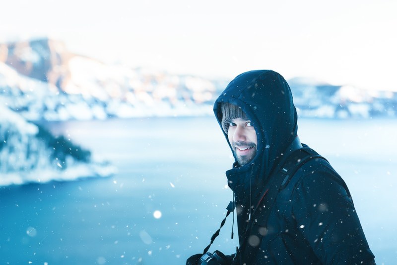 a man smiling at the camera while walking alongside crater lake taken during the winter, snow encounter 4k