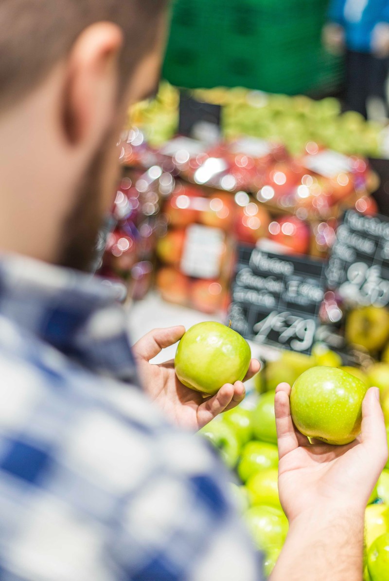 a man holding two green apples comparing them before purchasing them at a grocery store, apples to apples 4k
