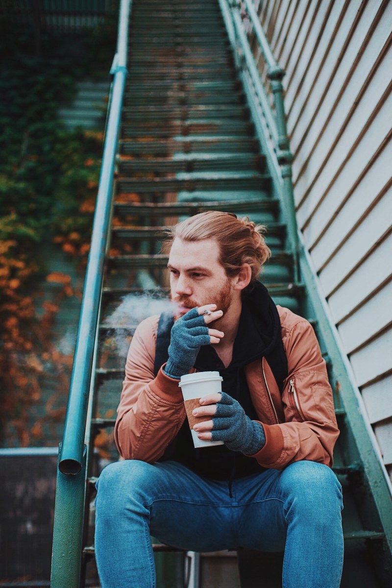 hipster man with a man bun drinking coffee on a staircase, lost in the fall 4k