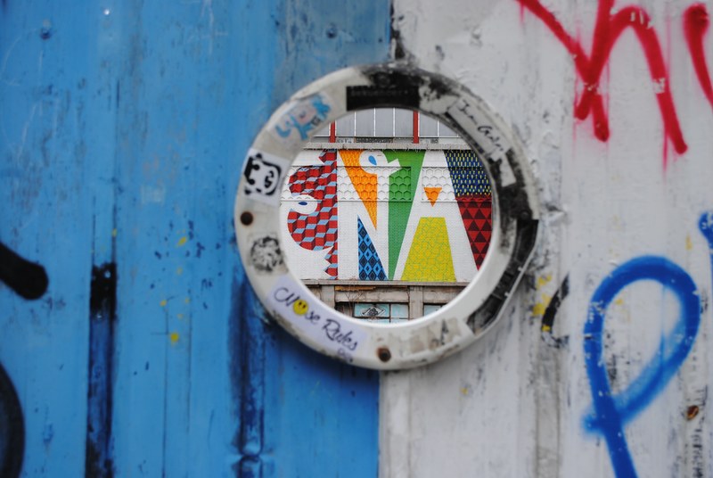colorful graffiti typography in round window surrounded by graffiti tags at mercado de la cebada, hole in graffiti wall 4k