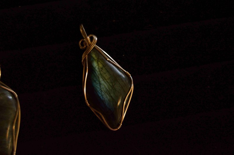 a gemstone pendant wrapped in a copper wire against a black background, twisted wire jewelry 4k