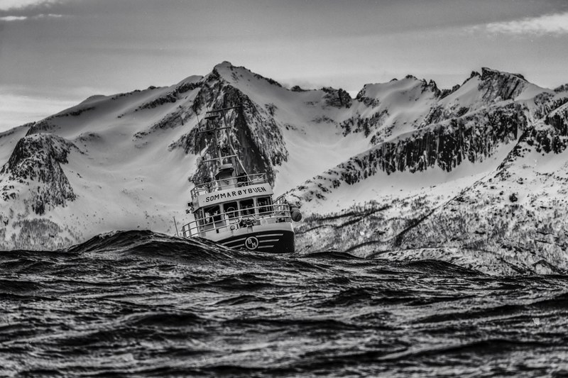 black and white shot of ship sailing in rough waters with snowy mountains behind, ship in rough waters 4k