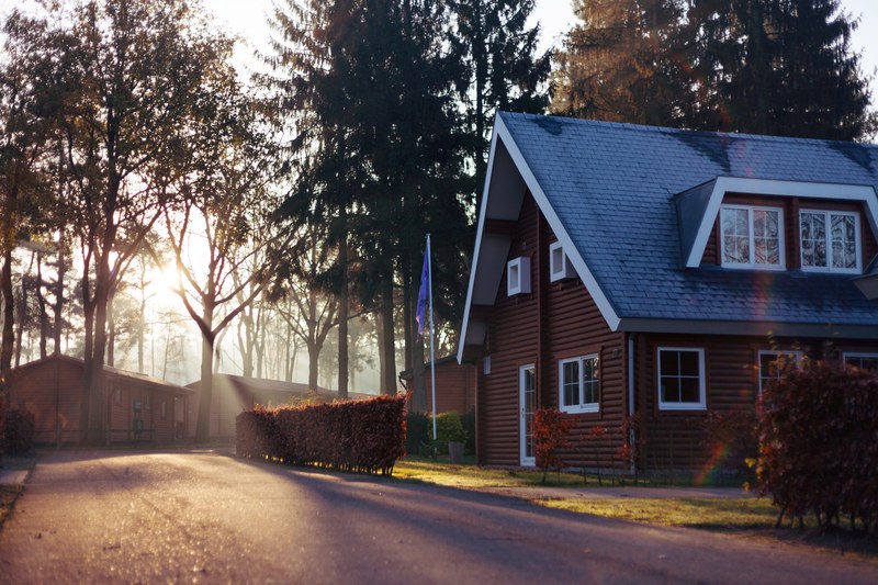 brown house with blue roof in front of trees with rays of the setting sun streaming through them, brown house blue roof 4k