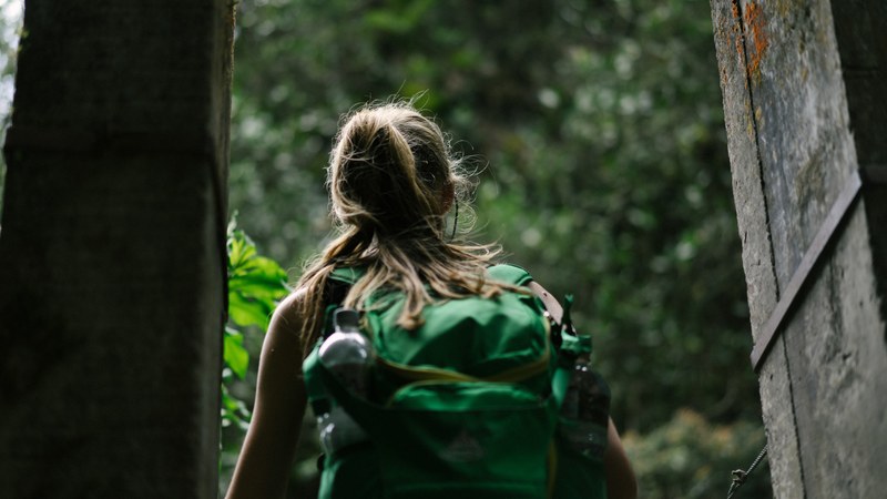 a woman with a ponytail green backpack and water bottle walks outside through wood doors, woman walks through wood doors 4k
