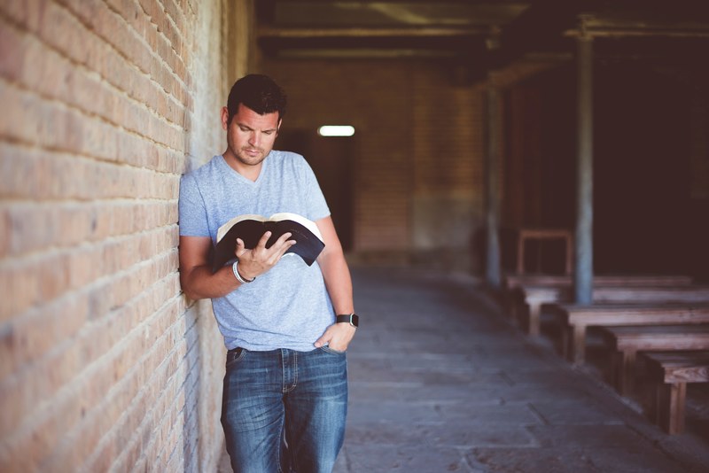 a man leaning against a wall outside while reading a book, _man reading outside 4k
