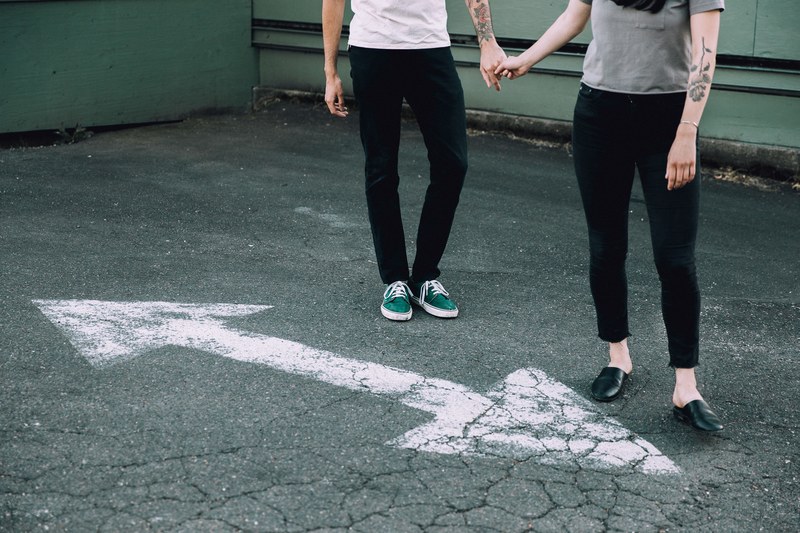 a couple holding arms while standing near white arrows pointing both ways, _couple holding hands 4k