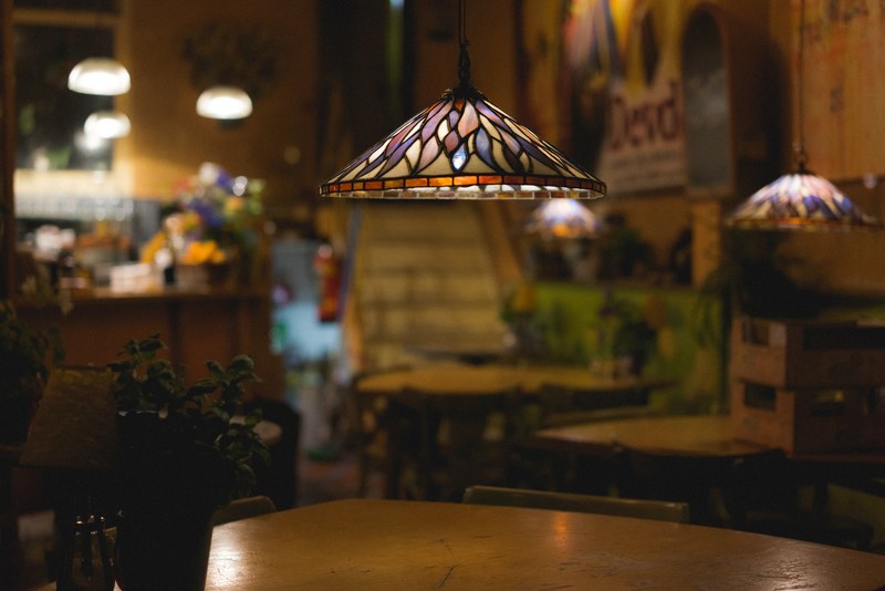 indoor hanging lamp lights and wooden table in cozy bistro restaurant interior in amsterdam, stained glass lamp over table 4k