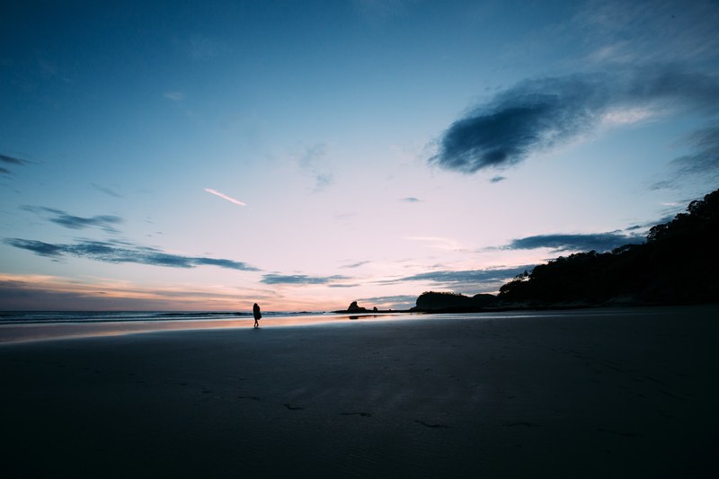 dark beach shot with bright blue sky at sunrise or sunset one silhouette person walking along the sand at playa maderas, walking along the beach in the dark 4k