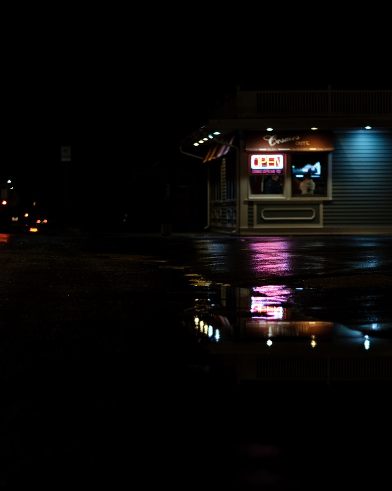 a store in the dark and a puddle reflecting the neon lights from the storefront window, storefront neon reflection 4k