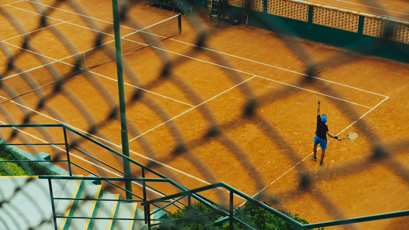a tennis player serving the ball in a court seen through a wire fence, tennis serve 4k