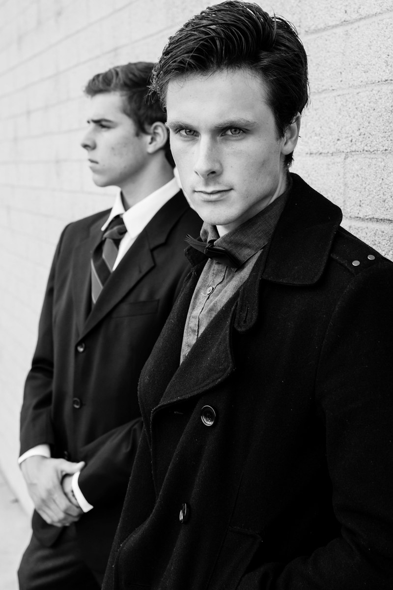 a black and white shot of two young men in formal attire near a wall, two elegant men near a wall 4k