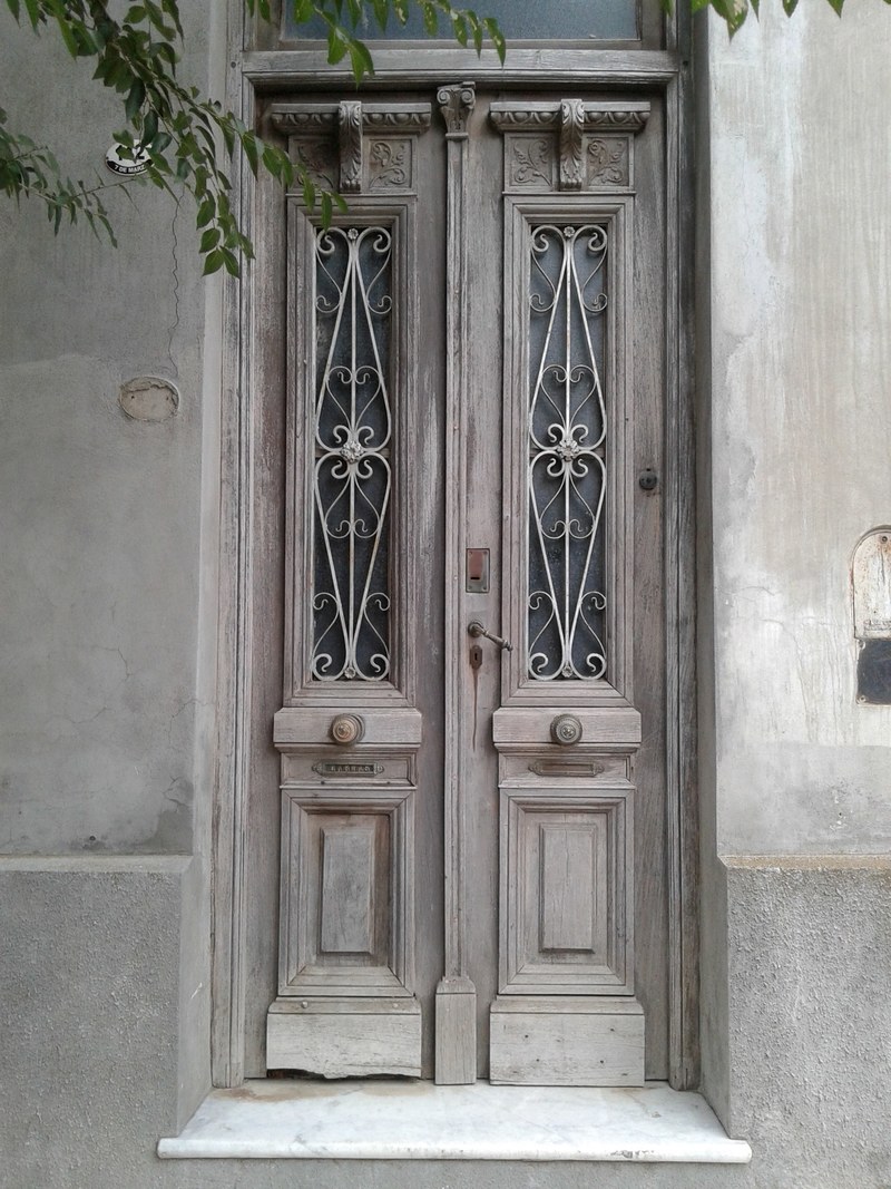 old vintage door with light wood and tall decorative glass windows on a tan building, visiting old cities 4k