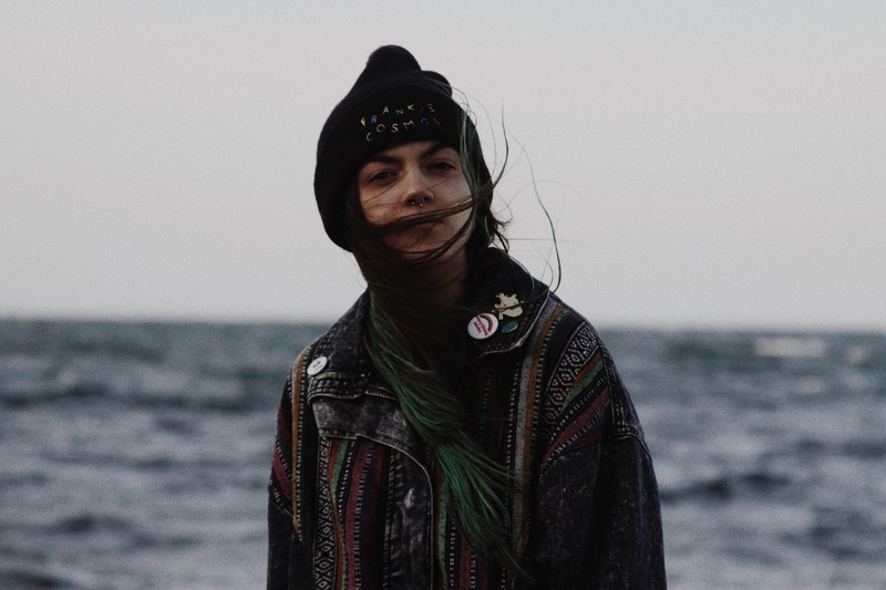 a woman in a hat coat and pins stands by the ocean with her hair blowing, woman with blowing hair 4k