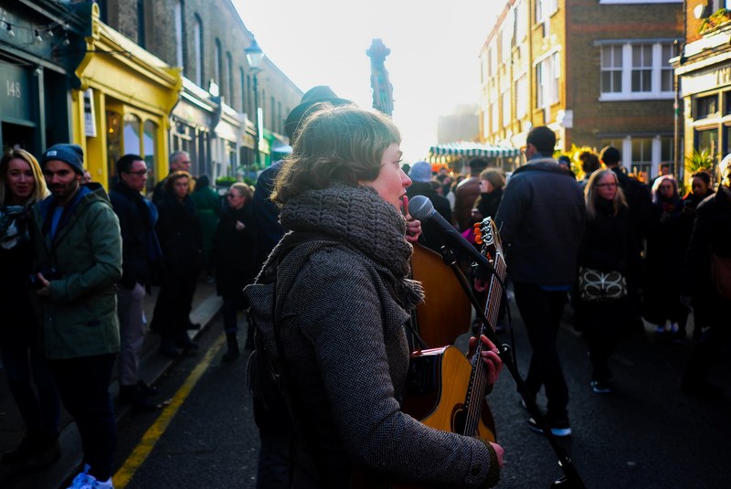 a woman playing acoustic guitar and singing into the microphone on a crowded street, and sing 4k