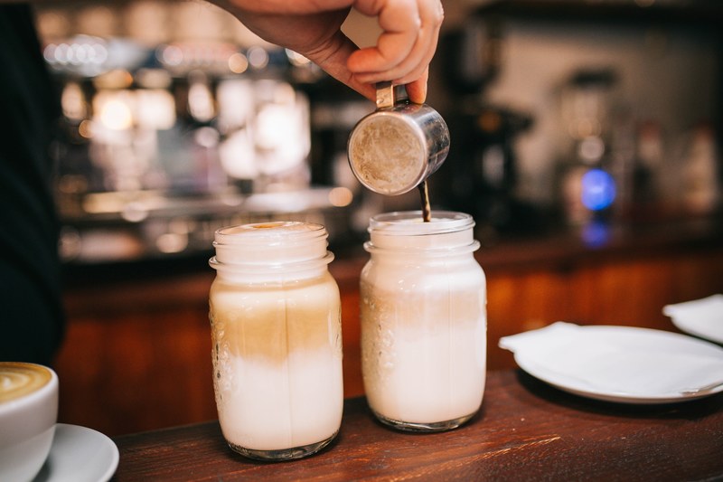 a person pouring coffee into jars with foamed milk, coffee room 4k