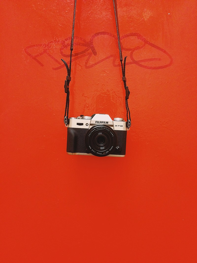 black fujifilm camera and straps in front of red surface with graffiti, hanging by a strap 4k