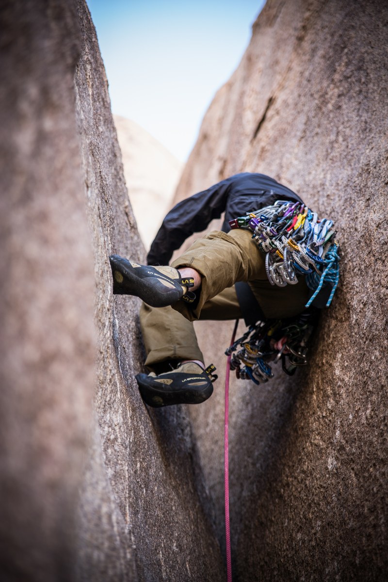 a rock climber scaling between two massive rocks and attached to a harness, lou leading 4k