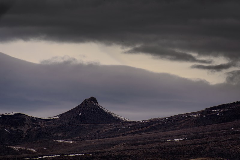 a jagged mountain peak crowns the horizon under thick clouds, lone mountain under clouds 4k