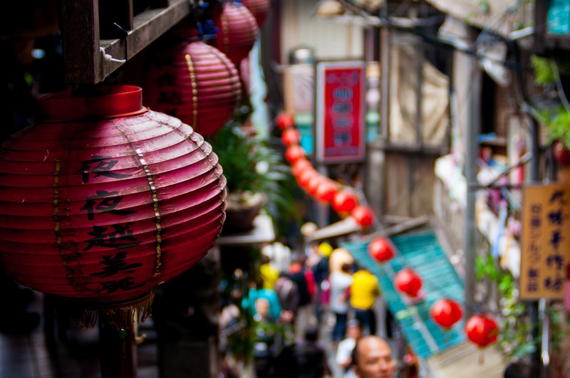 the macro view of chinese lanterns placed on walls and a blurry view of people walking in a market road in jiufen old street, _chinese lanterns in market 4k