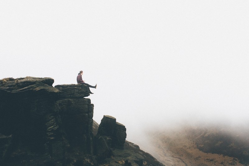 hiker sits on the edge of a rocky cliff after climbing in dovestones edge, within the clouds_ 4k
