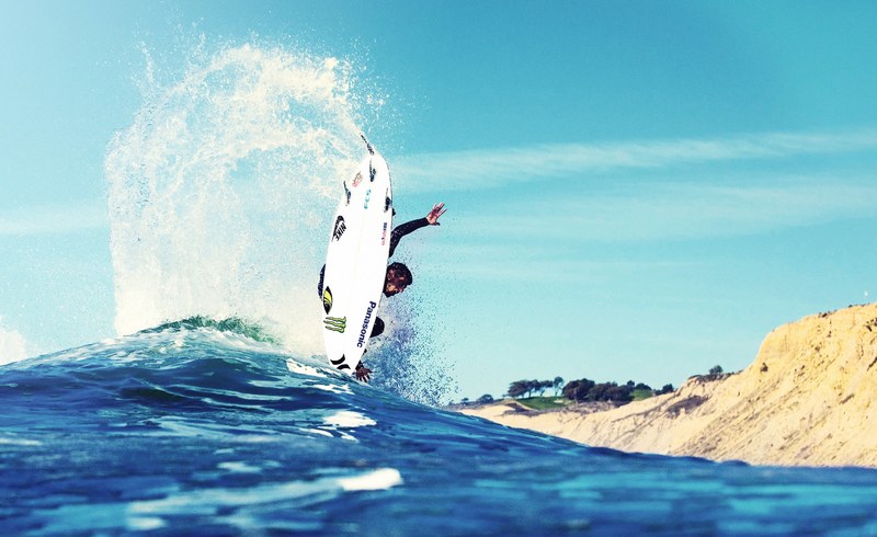 an artistic shot taken from the water of a surfer performing a trick in the sea with the beach visible to the right sidi mghait, surfing trickster 4k