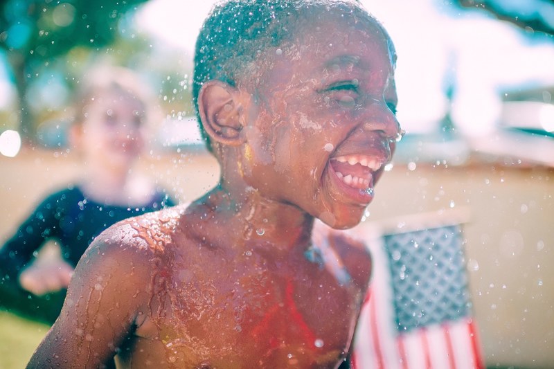 a boy laughing and running through splashing water on a sunny day, boy laughs and splashes 4k