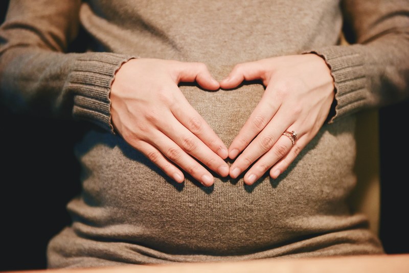 a pregnant woman in a sweater forming a heart with her hands on her belly, mom 4k