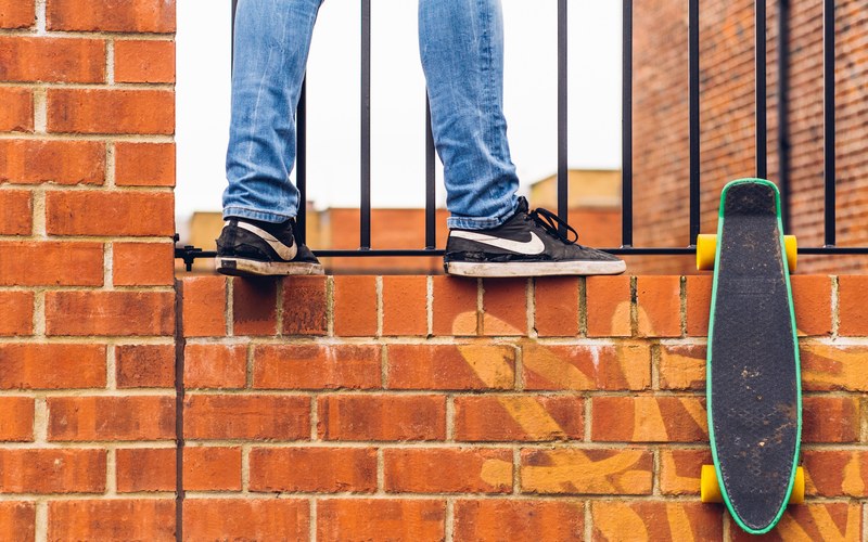 macro of a mans lower legs in jeans and nike sneakers standing on a brick wall with a black skateboard in sheffield, _tobys feet 4k