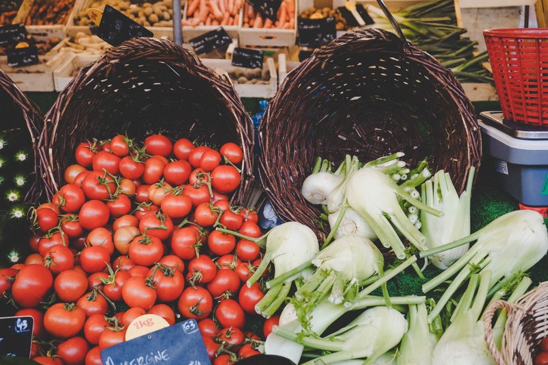 two baskets with tomatoes and fennels overflowing with other vegetables in the background, farmers market 4k