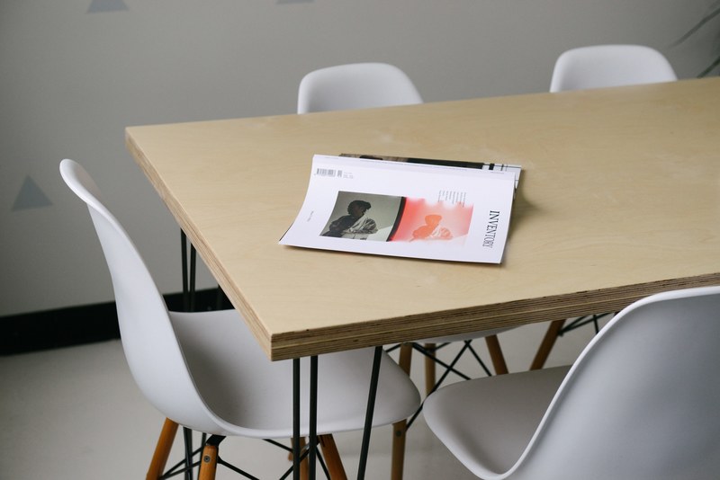 a business book turned over on a wooden table surrounded by chairs in a simple office setting, wooden table and chairs 4k