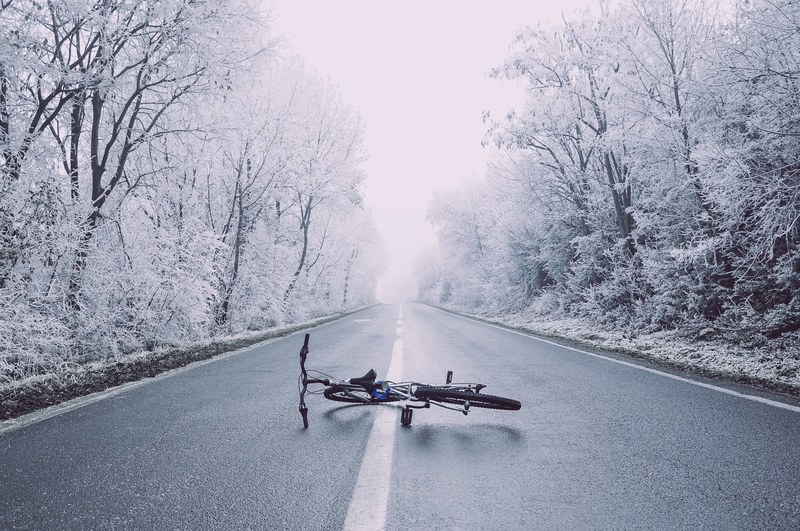 a bicycle in the middle of an asphalt road surrounded by trees covered in snow during winter in skopje, skopje winter road 4k