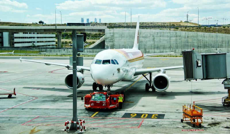 a white plane being pulled in from the runway by a vehicle with a developing city in the background, plane dragged on the tarmac 4k