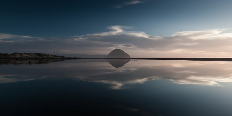 clouds reflected on the clear surface of a lake with a large hill on the shore, clear lake mirror 4k
