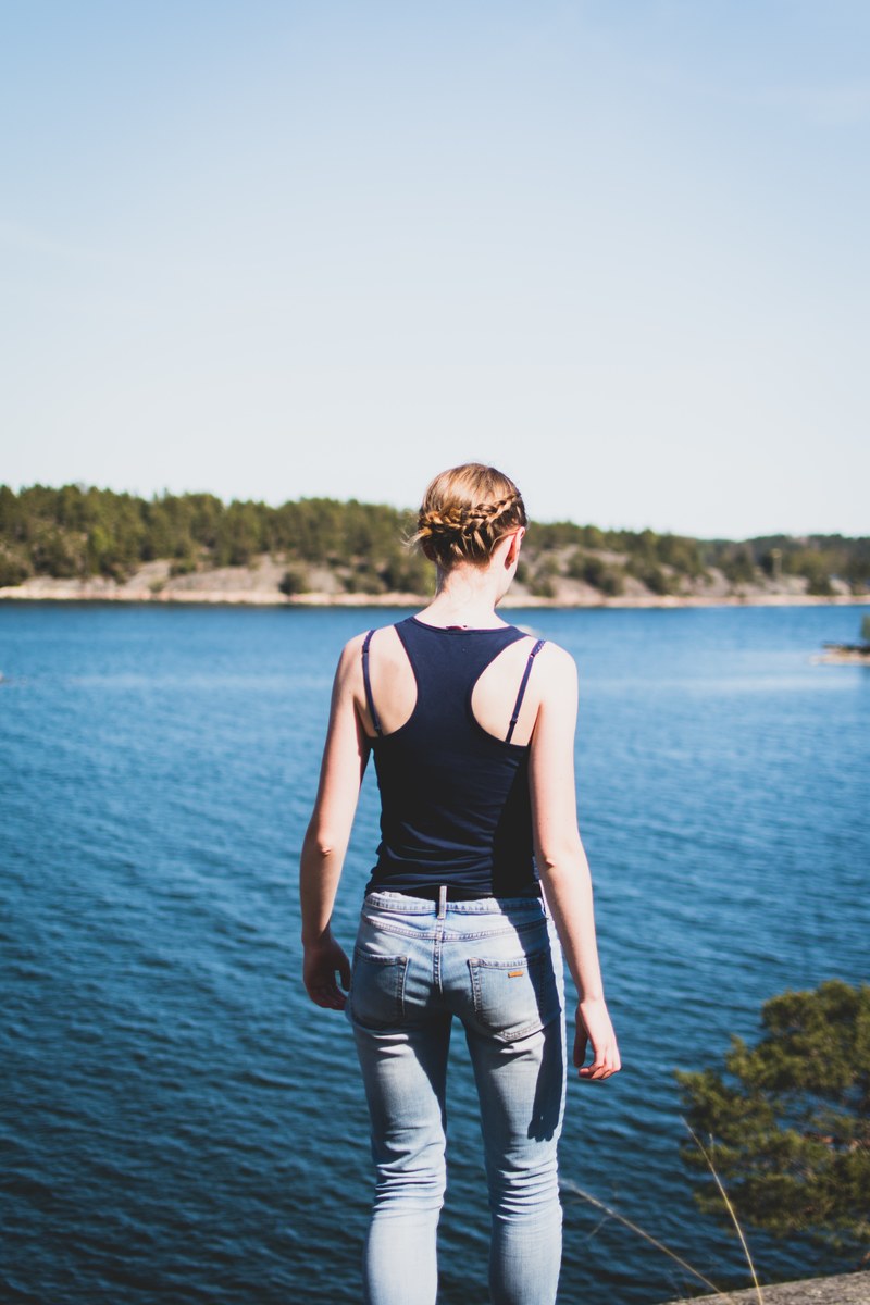 woman in jeans and a tank top walking near water at grind, woman near grinda water 4k