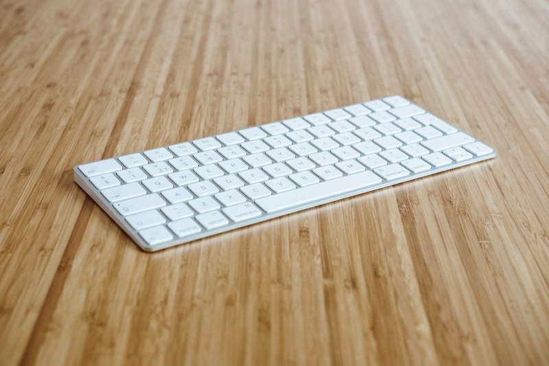 a white wireless apple keyboard on a wooden surface, the magic is in the keys 4k