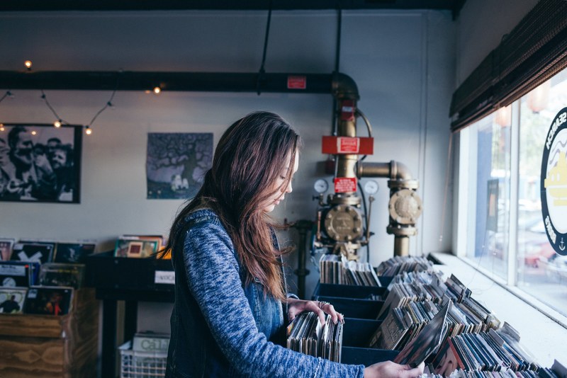 a woman browsing vinyl records in a record store, buying old records 4k