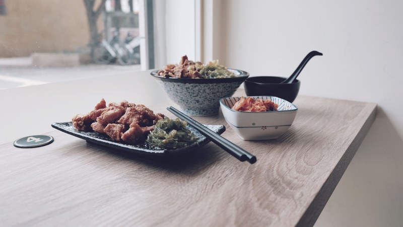 a dish consisting of deep fried meat with a side of kim chi and noodles on a numbered wooden table with assorted bowls and a set of chopsticks, dozo 4k