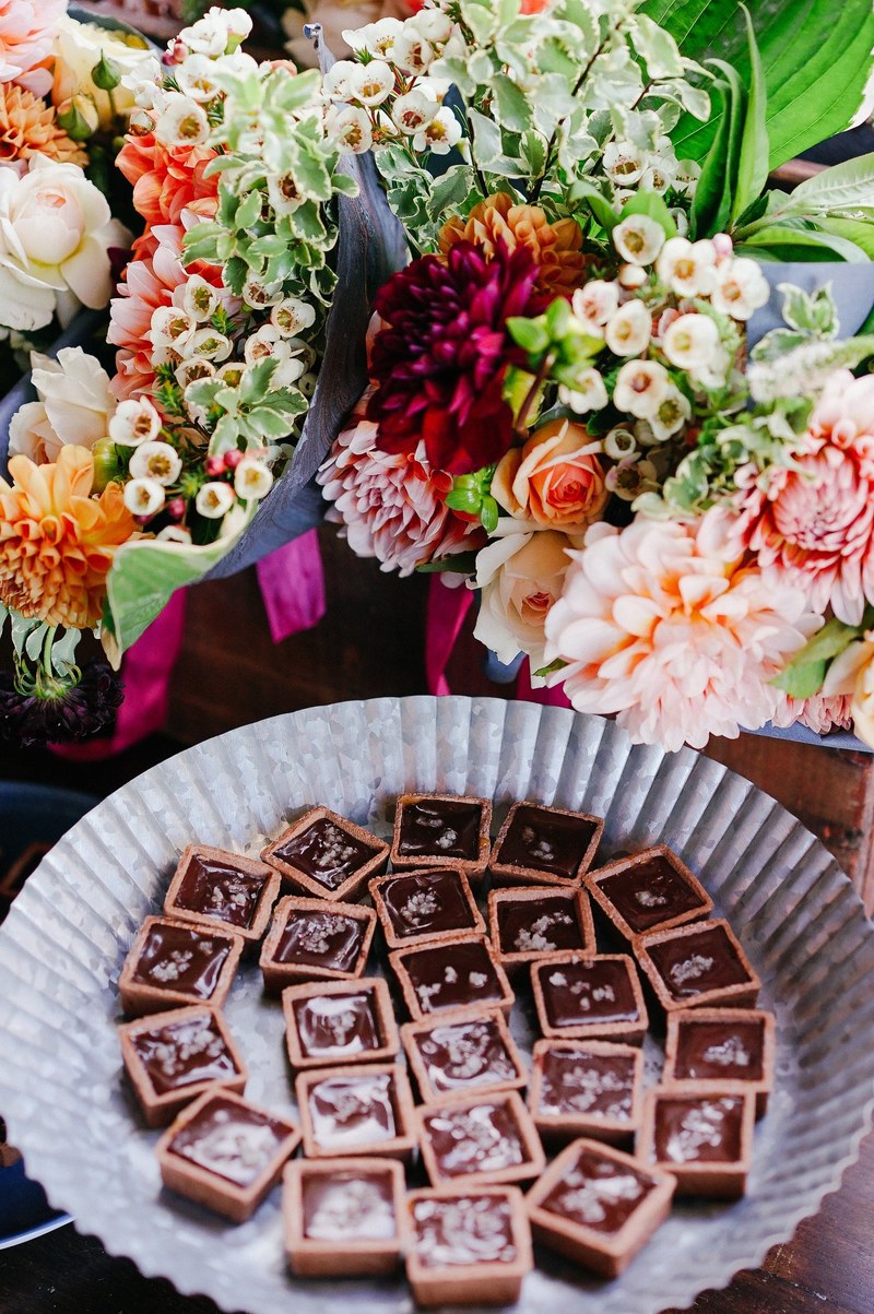 a paper plate with chocolate candy next to an arrangement of various flowers, sweet table 4k
