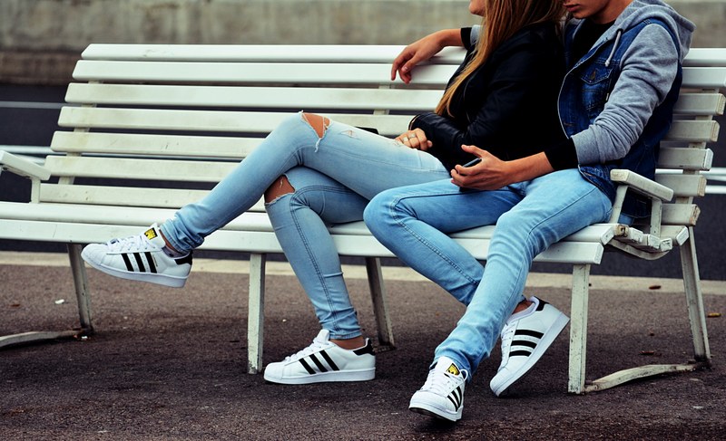 a man puts his hand around a woman in jeans sitting on a white bench outdoors, couple in jeans 4k