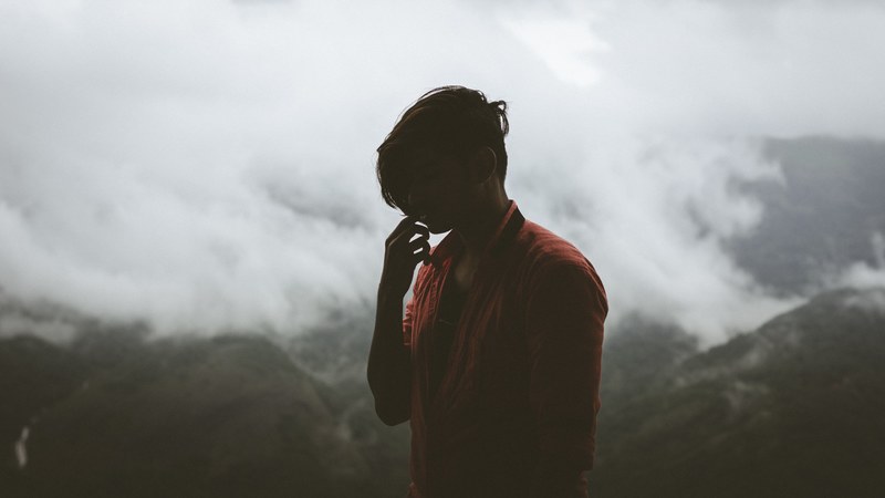 a person in silhouette holds a hand to their face in front of foggy mountains, like this forever_ 4k