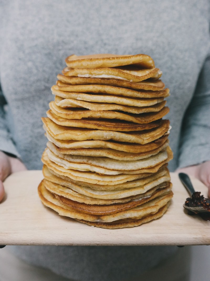 person holding a cutting board with a stack of homemade pancakes, brunch in bed 4k