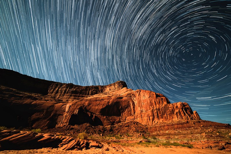 a blurry background image that perfectly captures swirling stars in a night sky over lake powell, cliff star trails 4k