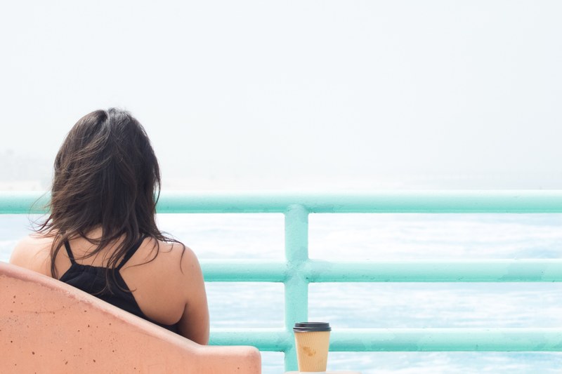 woman sitting alone with cup of coffee behind light blue railing at manhattan beach, woman sitting alone 4k