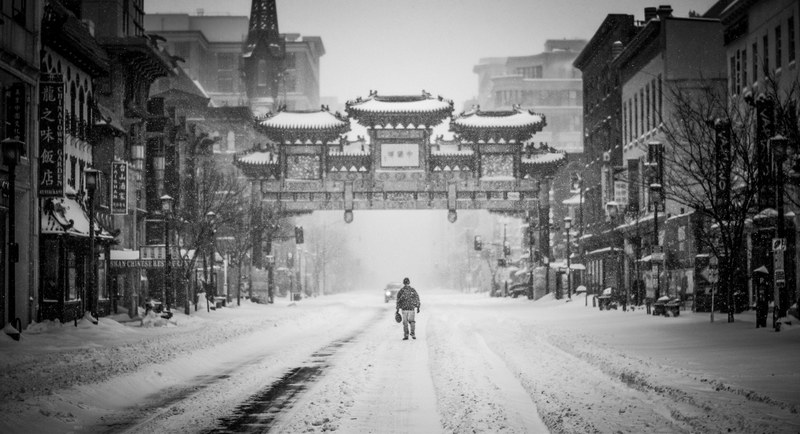 a man walking down a snow covered street in chinatown in black and white, a man in snowy chinatown 4k