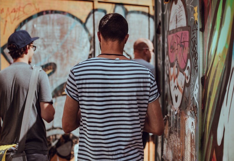 a man facing away in a striped t shirt aside brightly colored graffitied walls, city strollers 4k