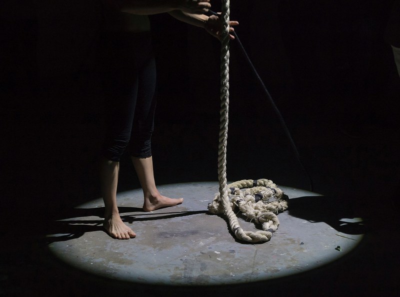a barefoot person holding rope under a spotlight, dancers feet and rope 4k