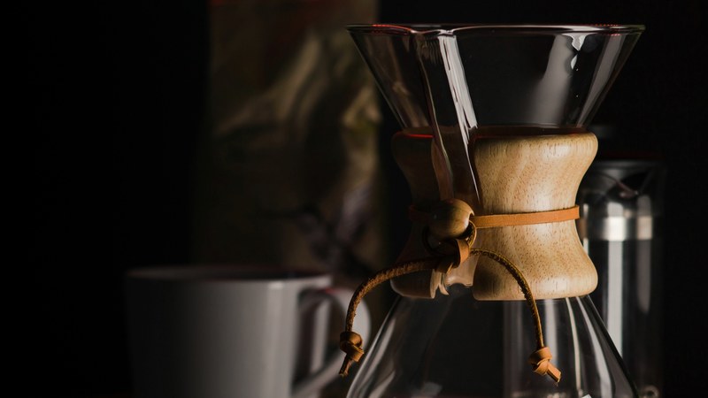 chemex pour over glass coffee maker next to ground coffee and a mug against dark background, chemex 4k