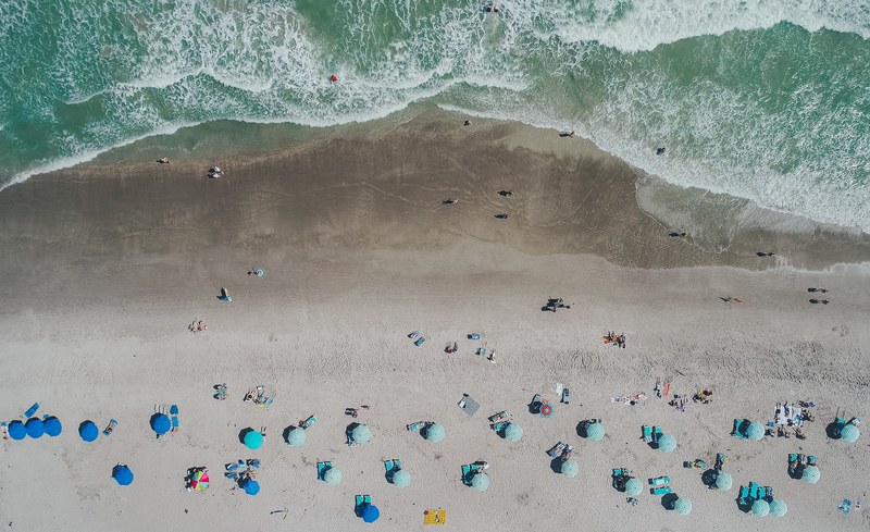 an aerial shot of vacationers on a sandy beach with blue umbrellas and deck chairs, clarity from above 4k